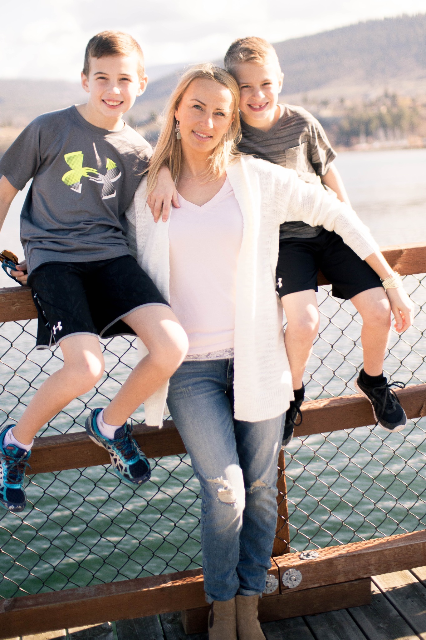 Outdoor family portrait of a mother with two smiling boys sitting on a waterfront railing
