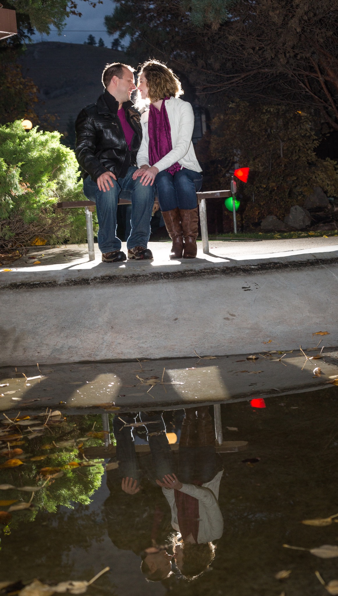 Couple sitting together at night, with their reflections mirrored in a puddle