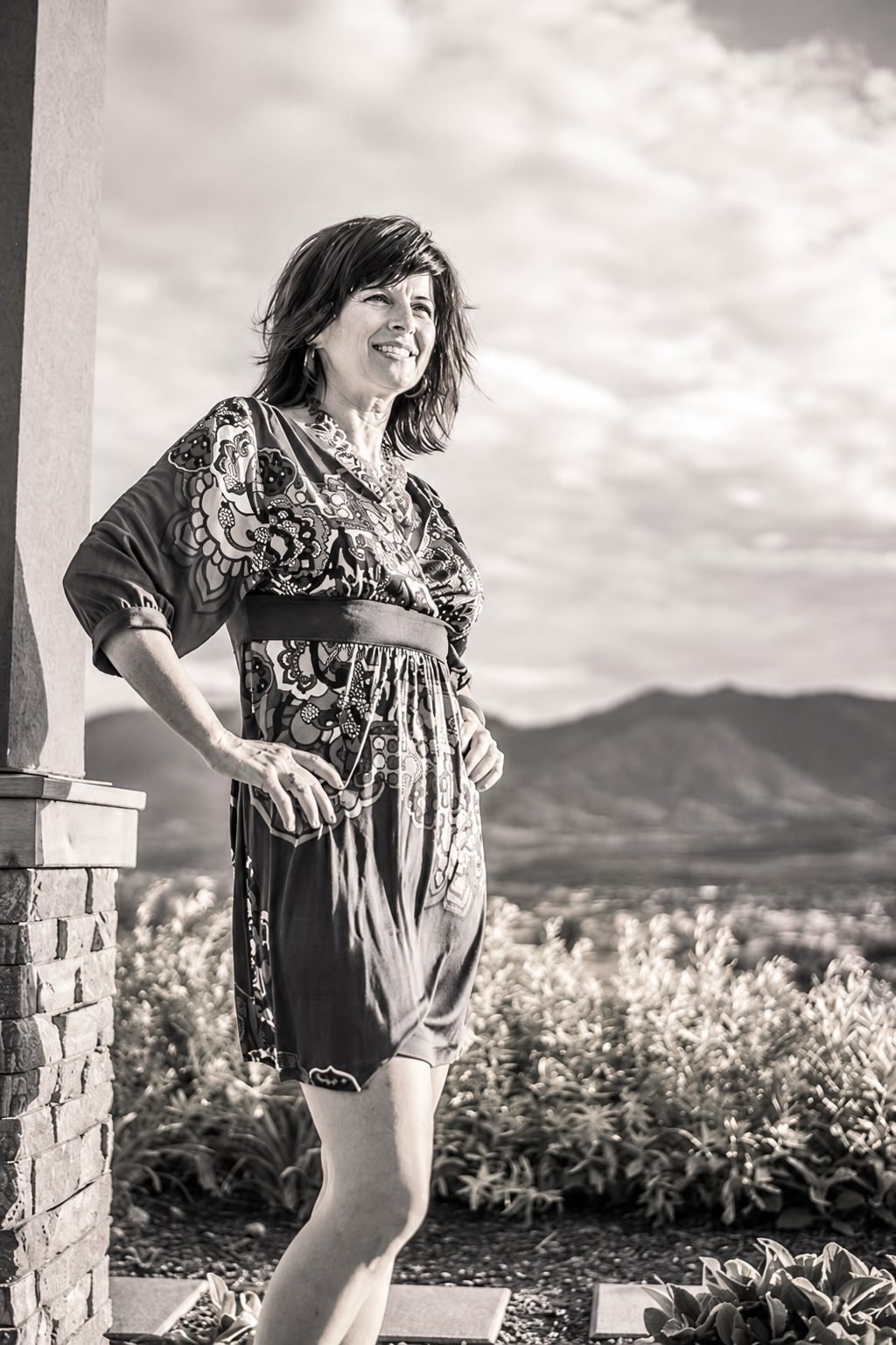 Black-and-white outdoor maternity portrait of an expectant mother in a patterned dress with mountains in the background