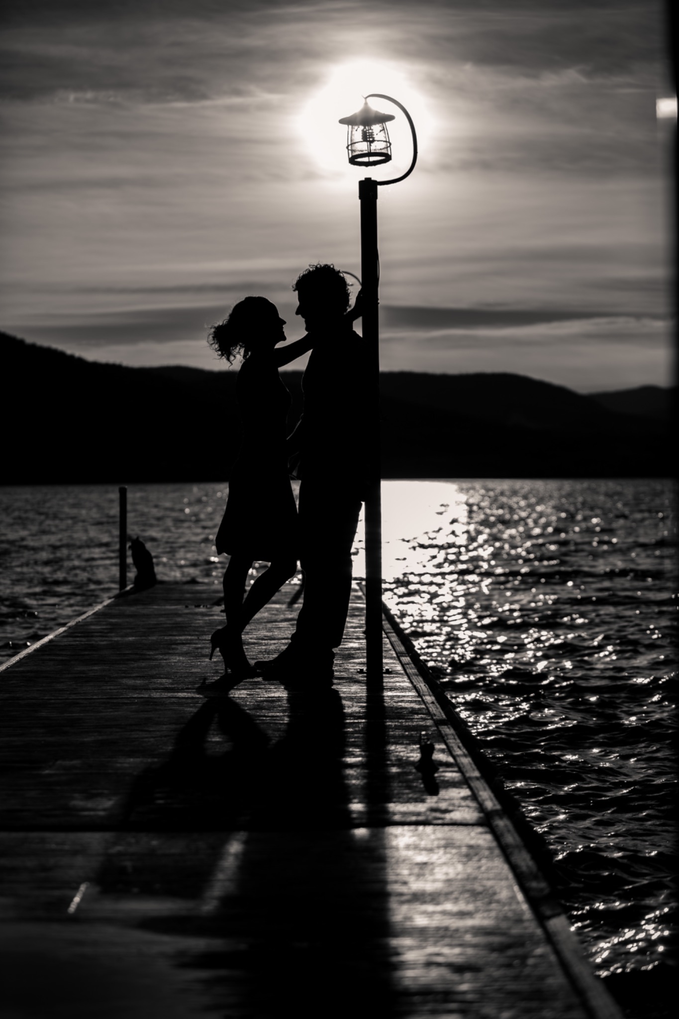 Moody black-and-white silhouette of a couple on a lakeside dock at sunset