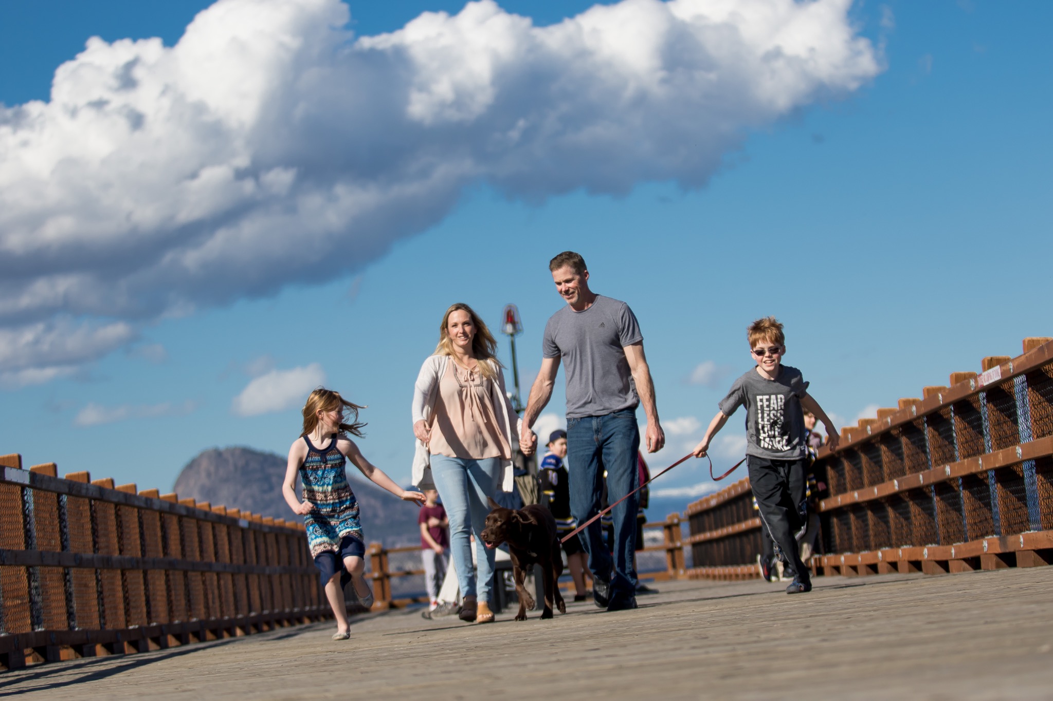 Family walking together with their dog across a wooden bridge under a blue sky