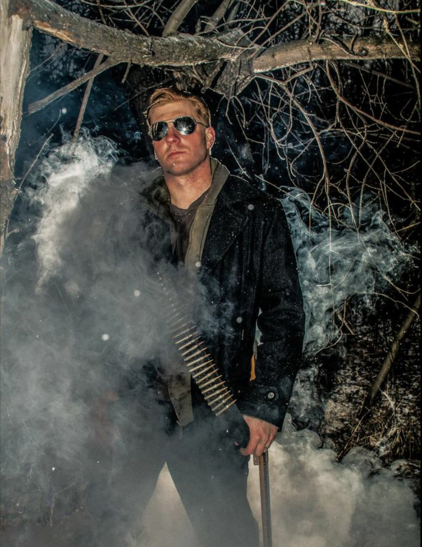 Dramatic outdoor editorial portrait of a man in aviator sunglasses surrounded by smoke and bare tree branches