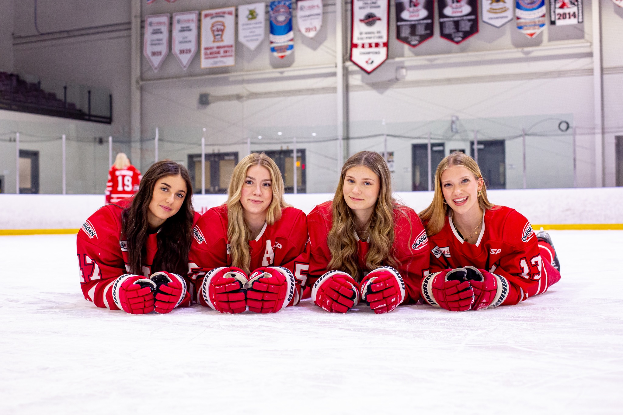 Four female hockey players in red Okanagan Hockey Academy jerseys posing on the ice