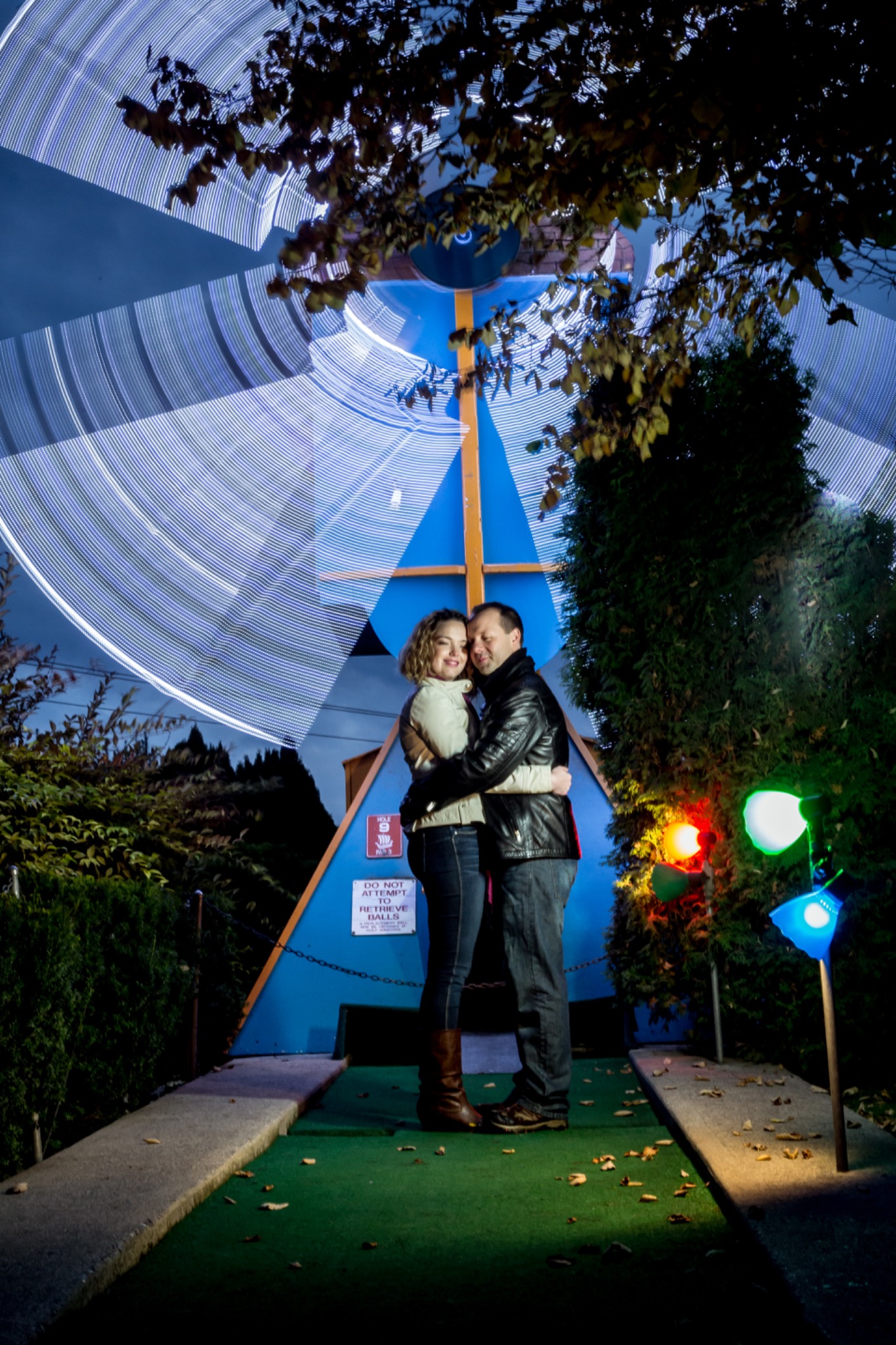 Couple embracing under colourful lights at an outdoor attraction after dark