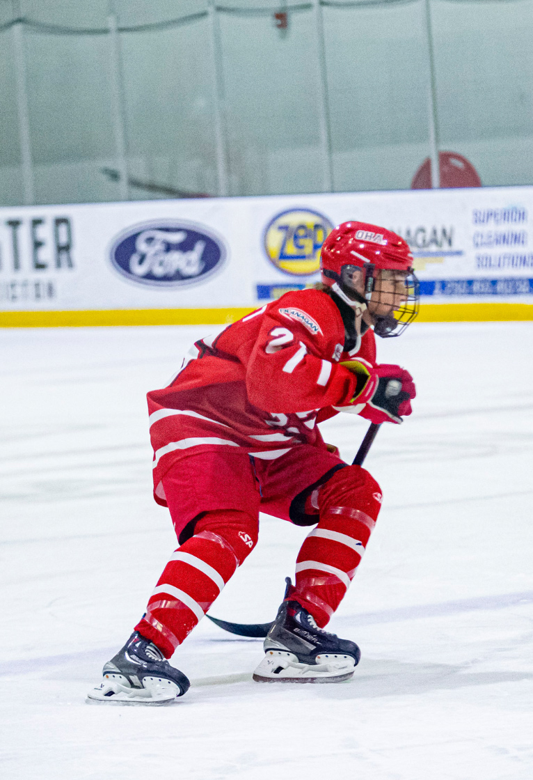 Okanagan Hockey Academy player in a red number 21 uniform skating with a hockey stick across an indoor ice rink
