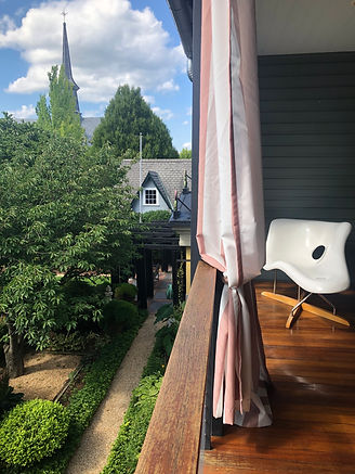 Image of the upstairs porch at the Peter Bullough Foundation with a modern chair overlooking leafy green trees in a courtyard