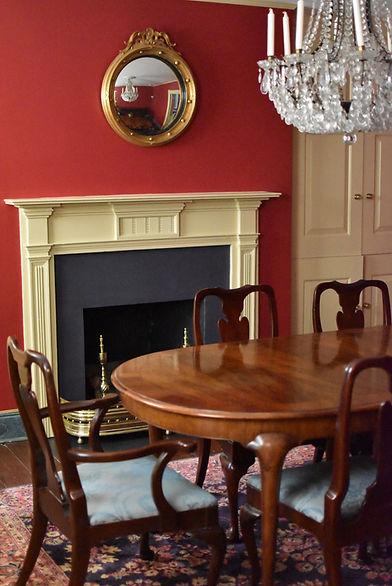 Dining room at the PBF residency with red walls, mirror, firepace, crystal chandelier, and table