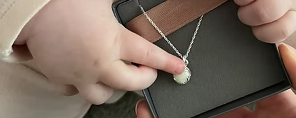 Breastmilk Silver Heart Pendant by Boobie Jewels being touched by an infant hand