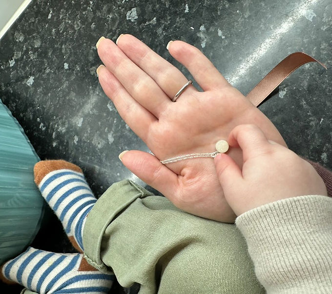 A breastmilk pendant necklace held by mother and child