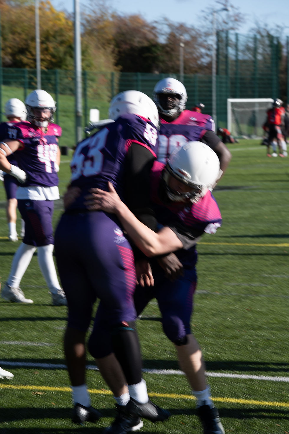 Two American football players in purple kits practising a tackling drill on a sunny outdoor pitch, captured with noticeable motion blur.
