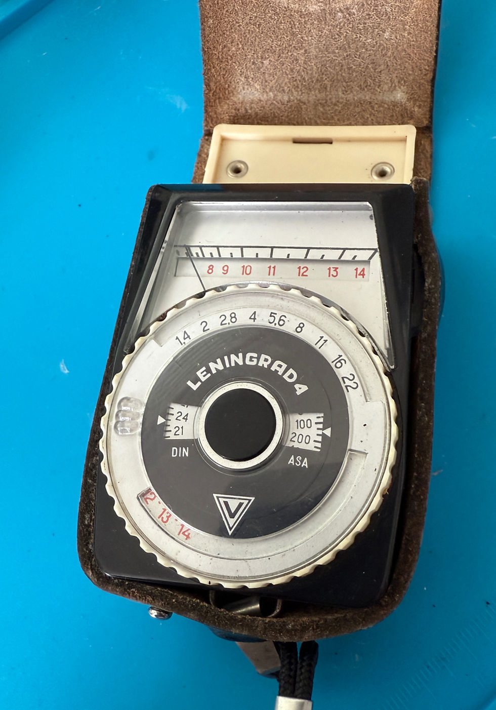 Soviet-era Leningrad 4 light meter with dial settings for ASA and DIN, shown inside its original leather case on a blue work surface.
