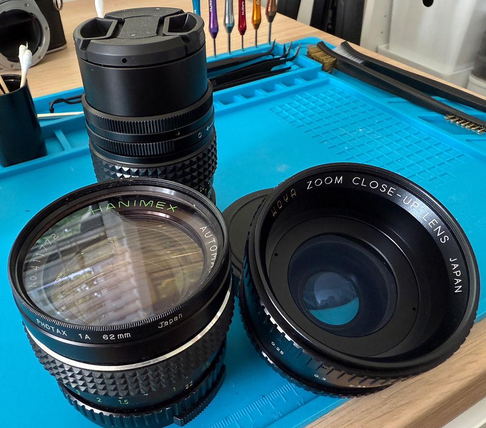 Selection of vintage manual focus lenses including Hanimex and Hoya, displayed with a Pentax ME camera body and repair tools on a blue mat.