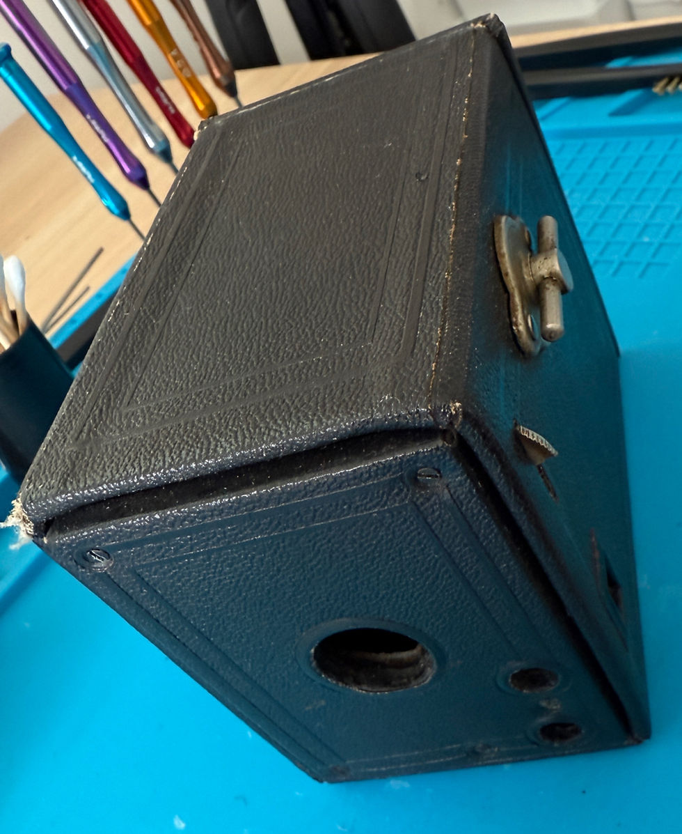 Old black box camera with metal latch and worn edges, positioned on a blue silicone mat near camera cleaning tools and screwdrivers.