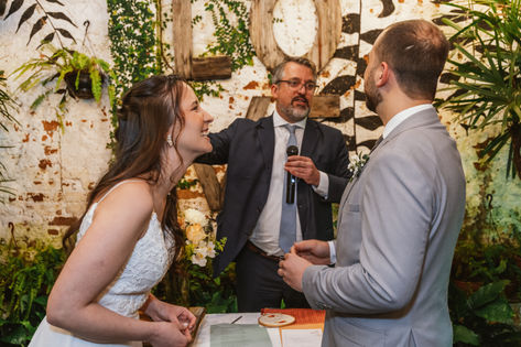 Casal ri enquanto troca as alianças durante casamento ao ar livre em jardim