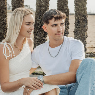 Ontspannen portret van Hannelore en Yentl zittend aan het strand tussen de houten golfbrekers.