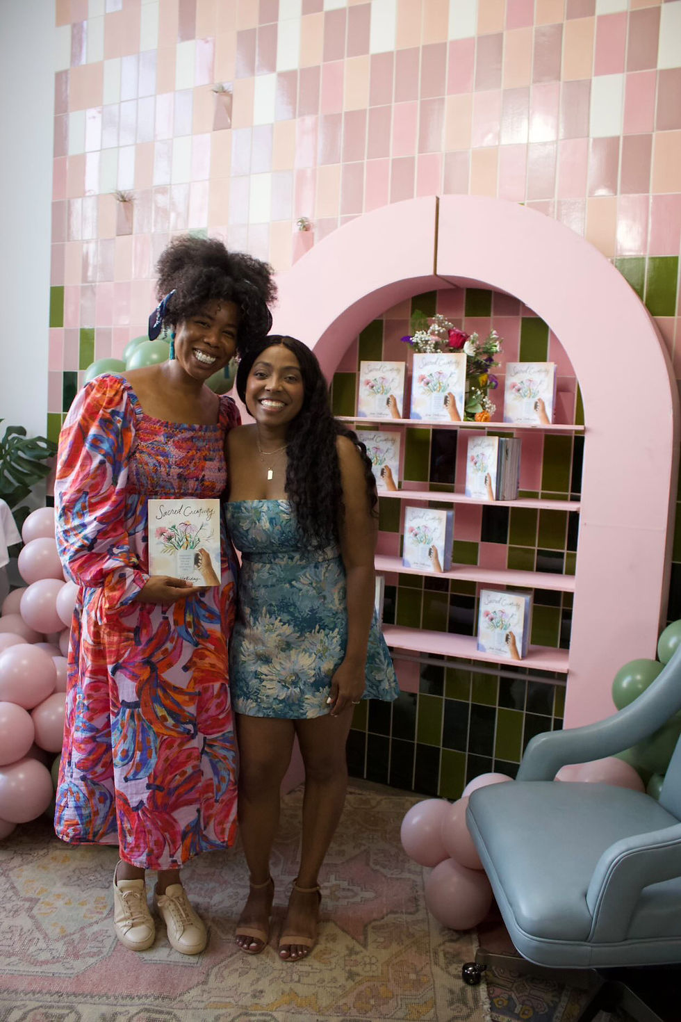 Shayla and Jena smiling in front of a book display at her book signing for Sacred Creativity
