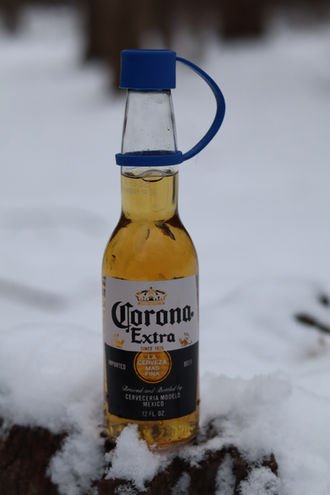 Corona beer bottle with blue Swig Essentials reusable bottle cap in snow.