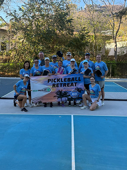 Group photo of 2026 participants wearing matching light blue shirts holding a banner that says Pickleball Retreat Costa Rica 2026