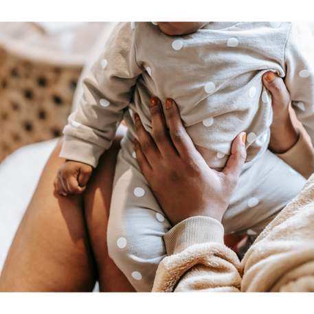 Baby in gray polka dot outfit held by an adult. Cozy, warm setting with soft lighting, creating a nurturing atmosphere.