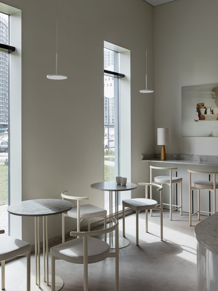 Minimalist café interior with sleek espresso machines, woven chairs, pendant lights, and neatly set tables.