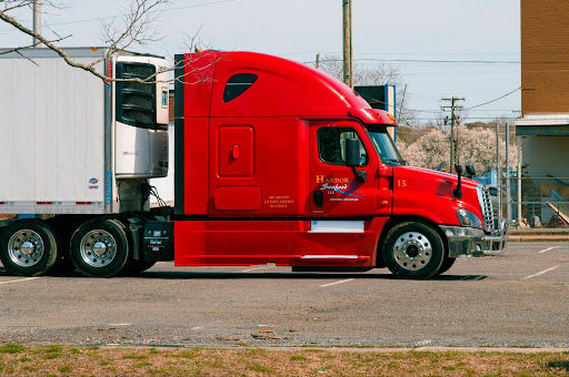 Red refrigerated semi-truck with white trailer parked on a street.