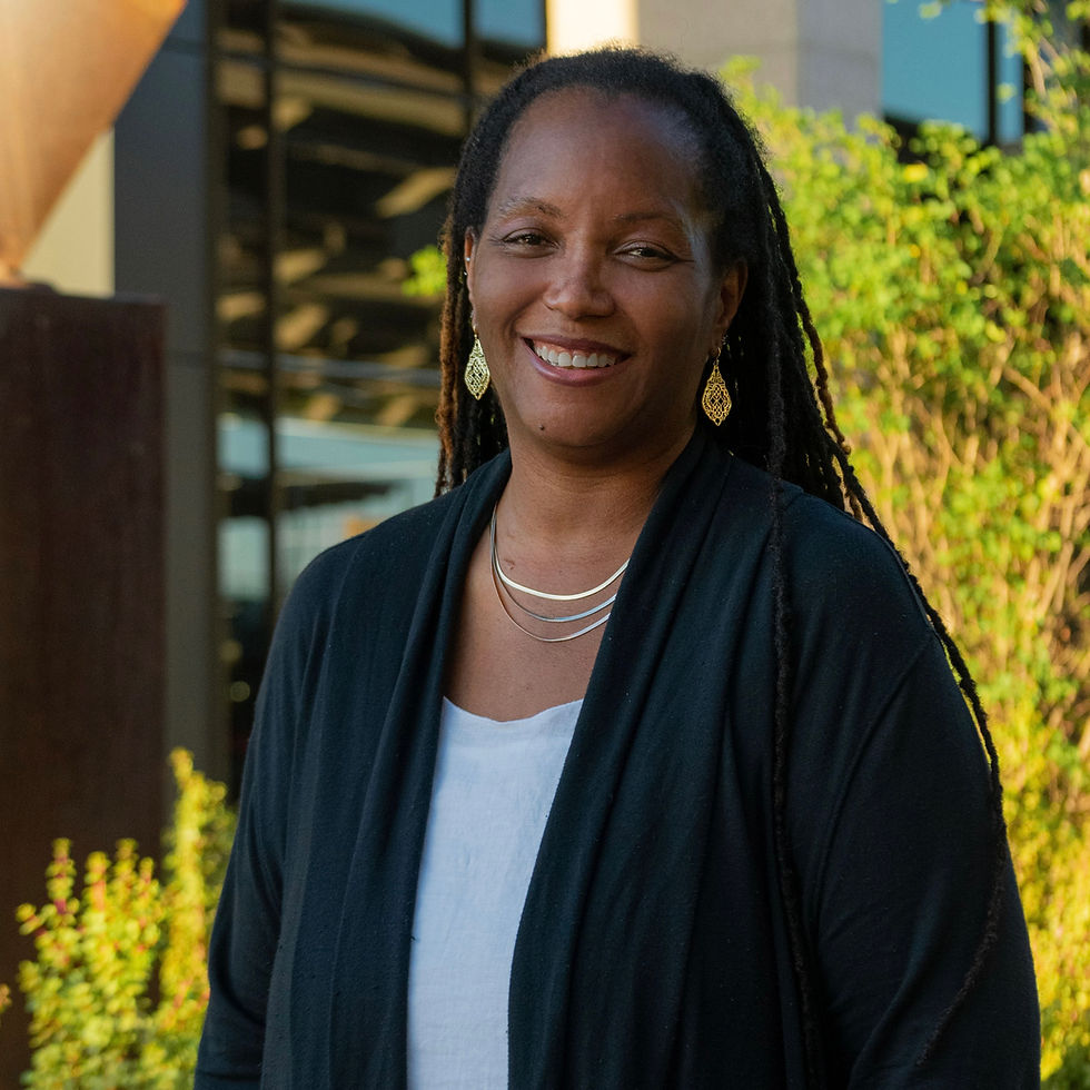 Eleesha Lewis, a professional voiceover artist, is smiling, standing outside with trees and a building in the background.