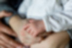 Depresia postnatală în era digitală: Provocările cuplului - Close-up of a baby's hand gripping an adult's finger. The baby wears a white, textured outfit. The scene exudes warmth and tenderness.