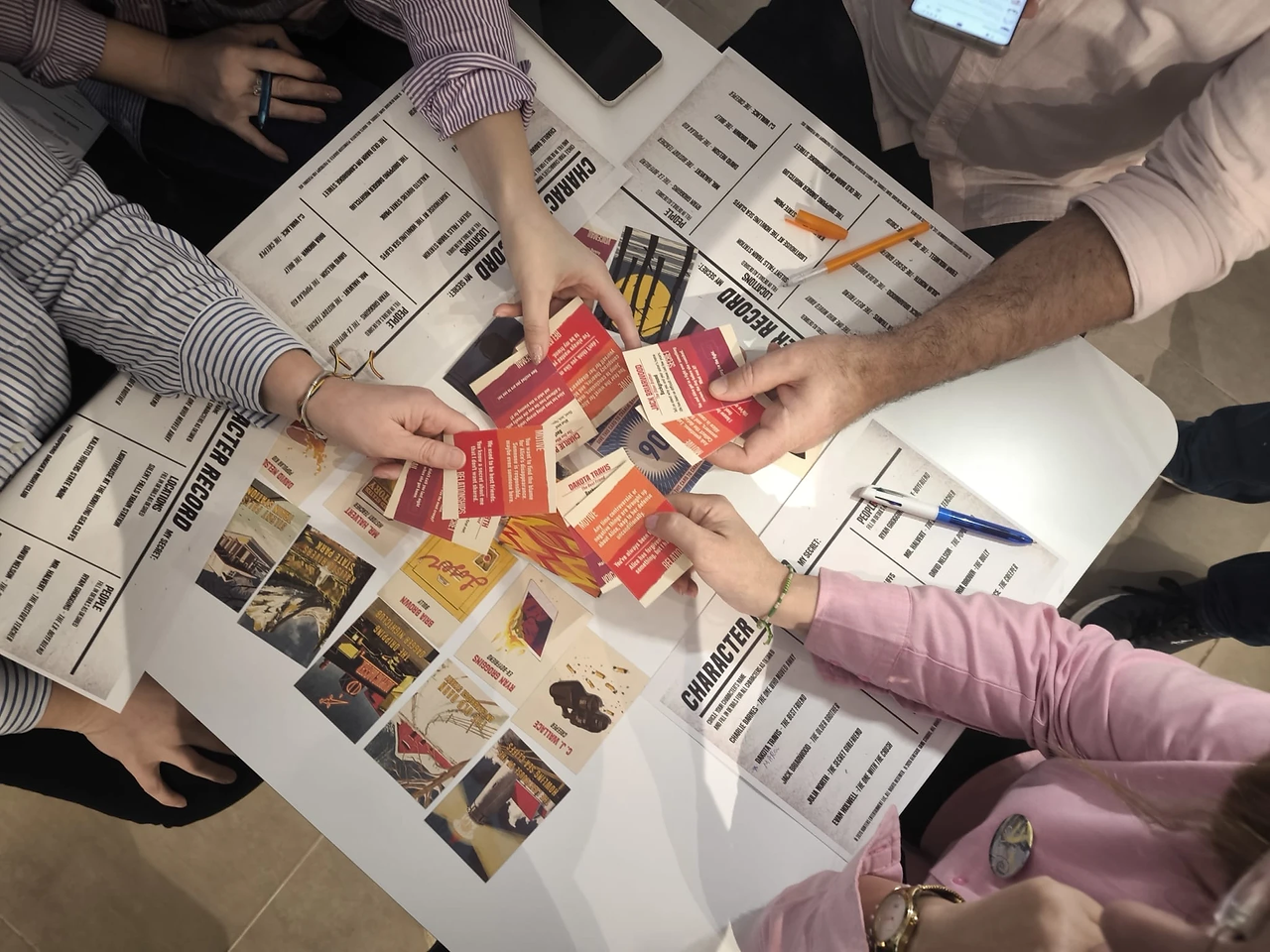 a table with games and tasks and 4 human hands showing off their cards