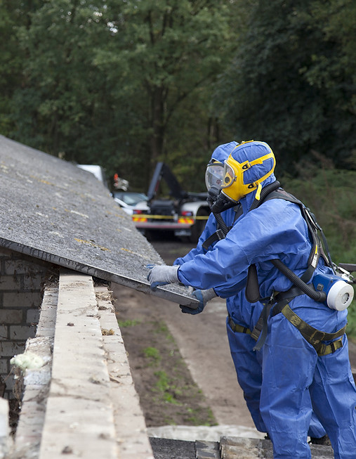 Technician in PPE safely removing asbestos insulation board from residential ceiling.