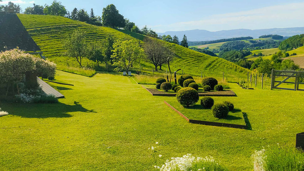 Begrünter Garten mit gepflegter Rasenfläche, formgeschnittenen Sträuchern und Weitblick in die Hügellandschaft.
