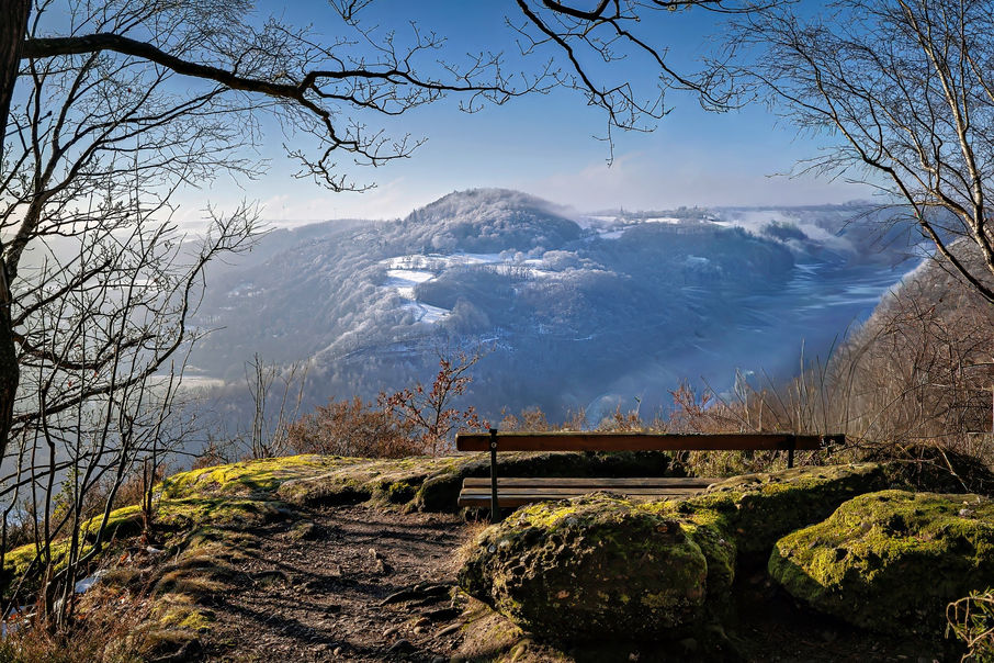 Sonniger Aussichtspunkt mit Bank und moosigen Felsen über dem teilweise verschneiten Rurtal bei Nideggen.