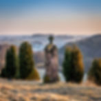 Old stone cross standing on a hilltop at sunrise, overlooking misty hills and fields — a symbolic and storytelling landscape scene.
