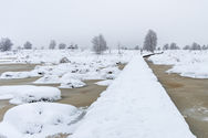 Schneebedeckter Steg über eine vereiste Seenlandschaft im Winter.