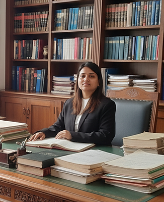 Professional lawyer seated at a wooden desk in a law office, wearing a black suit and white band, with law books, a gavel, an