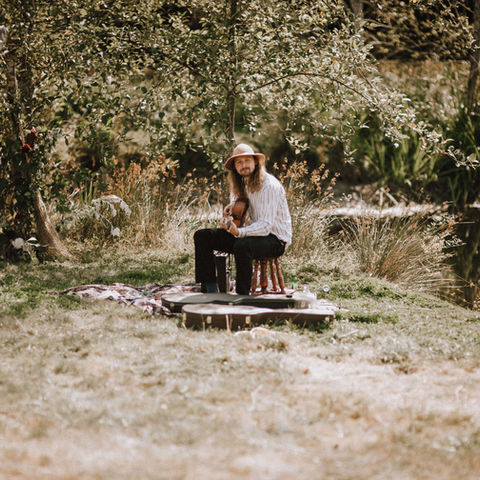 A man with a guitar sits on a bench near a pond and plays for the wedding party