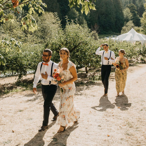 A wedding party procession walks between rows of fruit trees