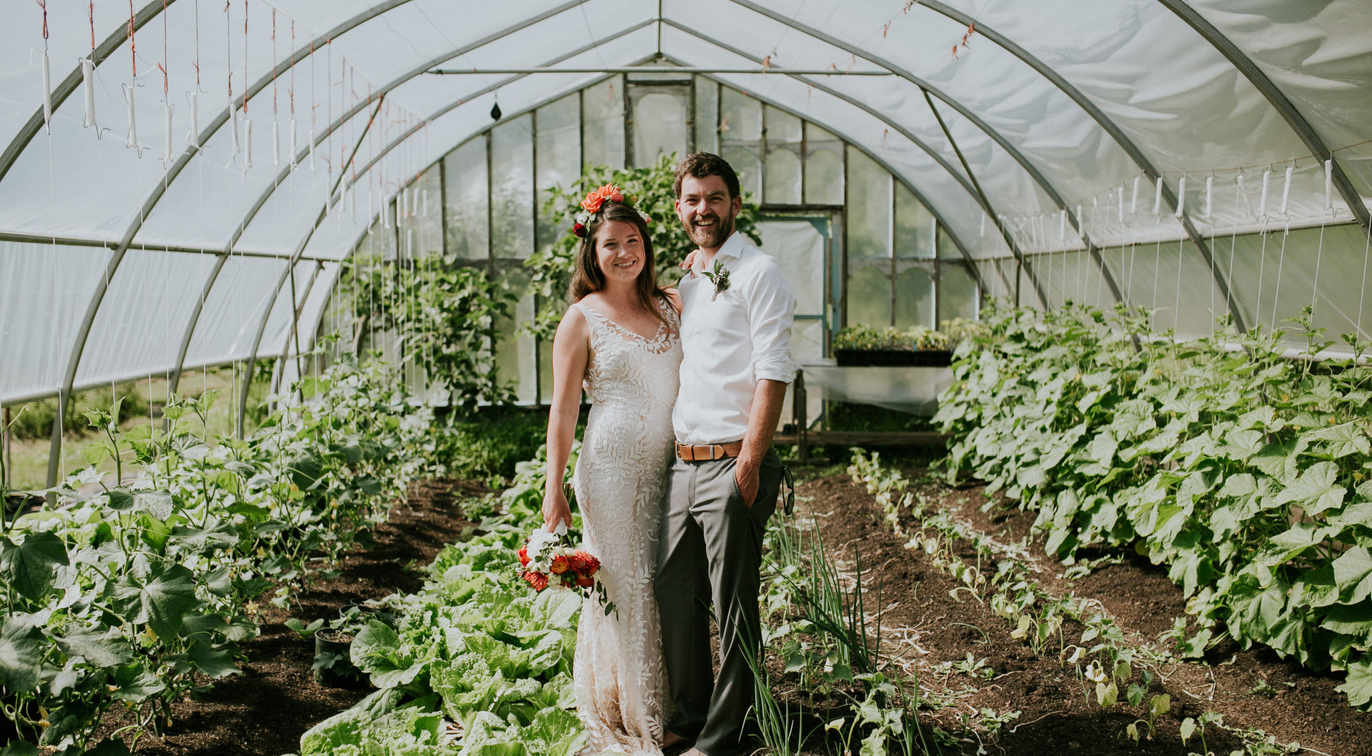 A couple poses surrounded by plants in a green house at this farm wedding venue