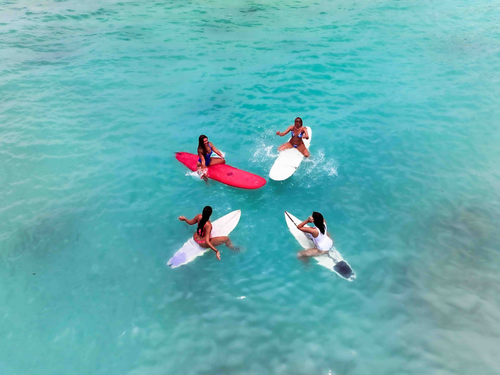 “Group of women on surfboards in turquoise waters, celebrating connection and sisterhood during Sundazed Retreats.”
