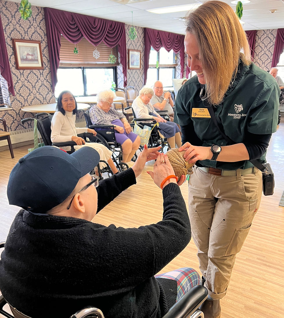 A resident at NBCC smiles while gently petting a small animal held by a petting zoo staff member during an outdoor visit.
