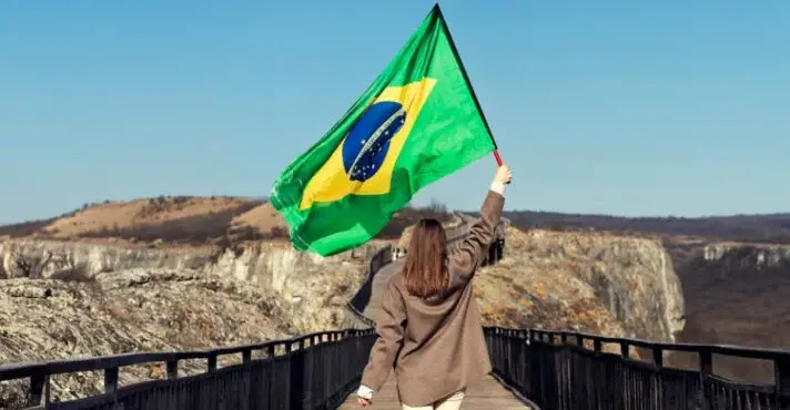 Mulher atravessando ponte segurando a bandeira do Brasil.