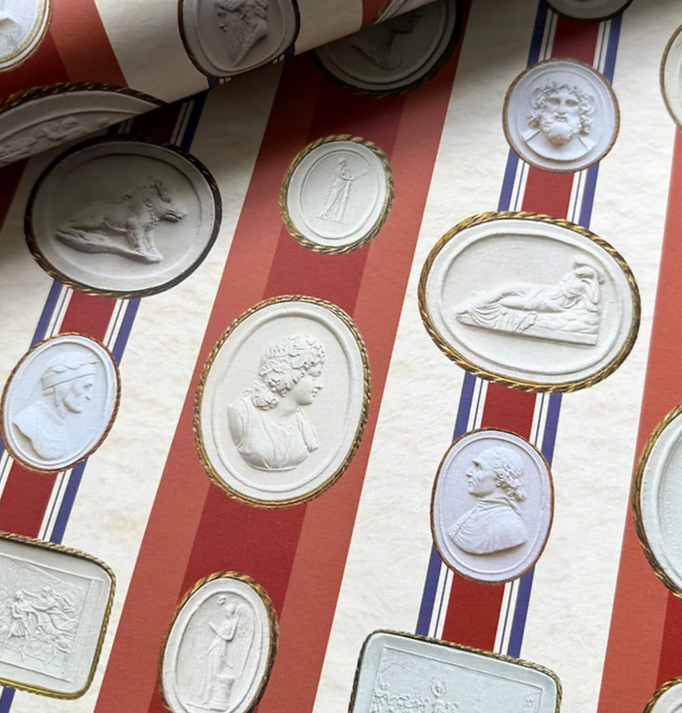 Cream wallpaper with red and blue stripes, featuring embossed classical portraits and scenes in oval and circular frames, creating a vintage feel.