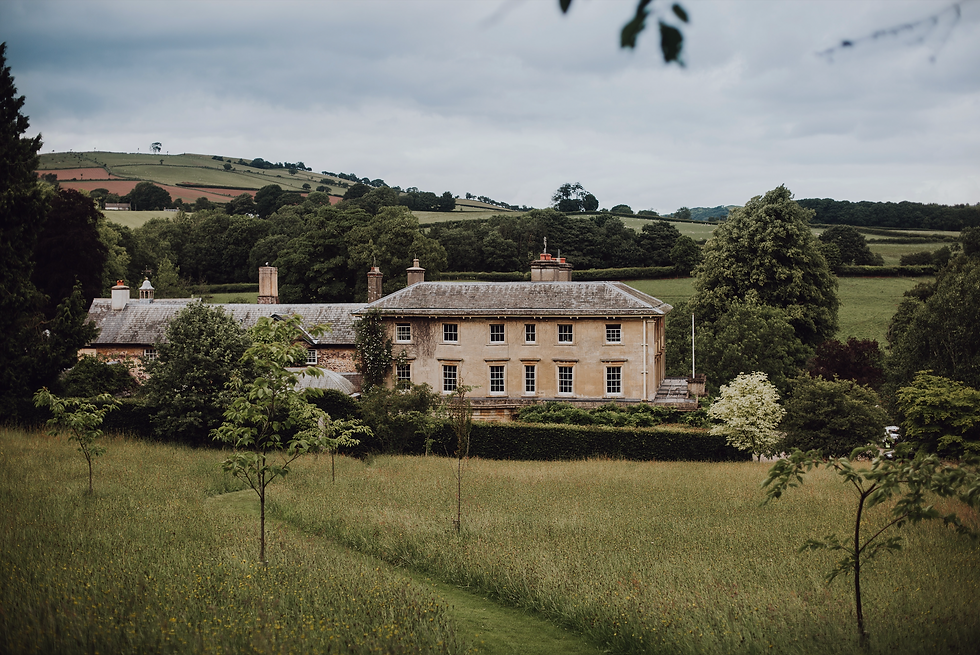Large country house surrounded by lush green fields and trees under a cloudy sky, conveying a serene and tranquil rural setting. Penpont Estate 