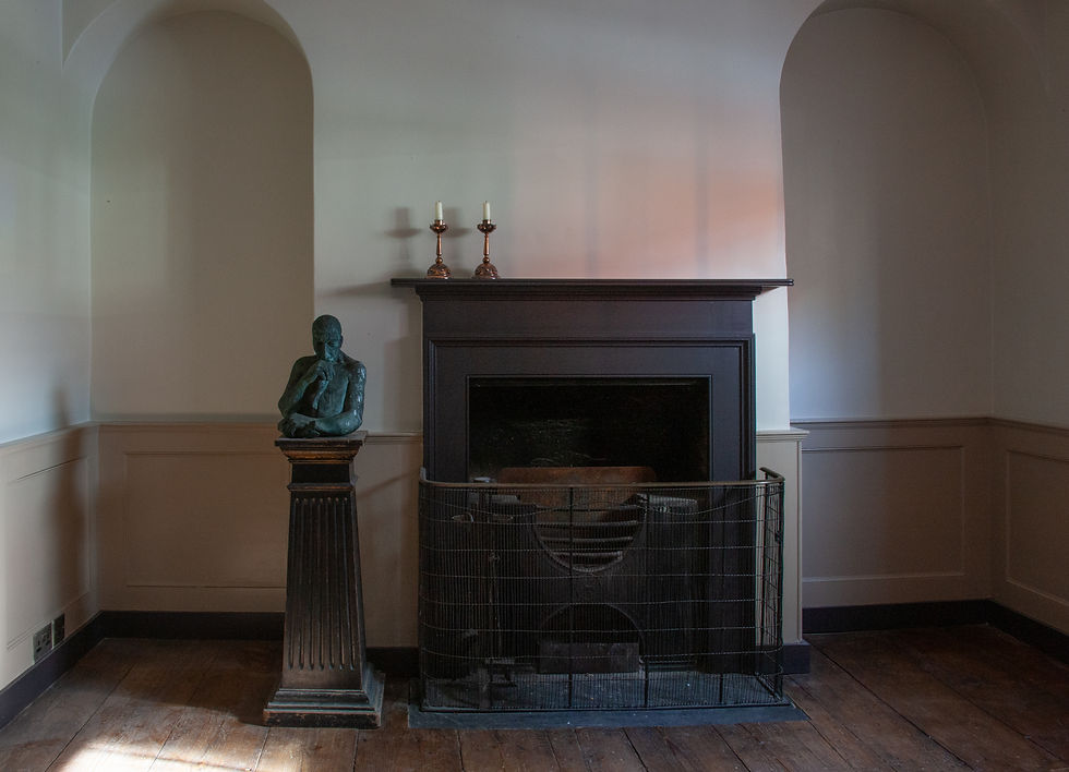 Bronze sculpture on a pedestal beside a dark fireplace with two candlesticks on top. The room has arched niches and wooden floors.