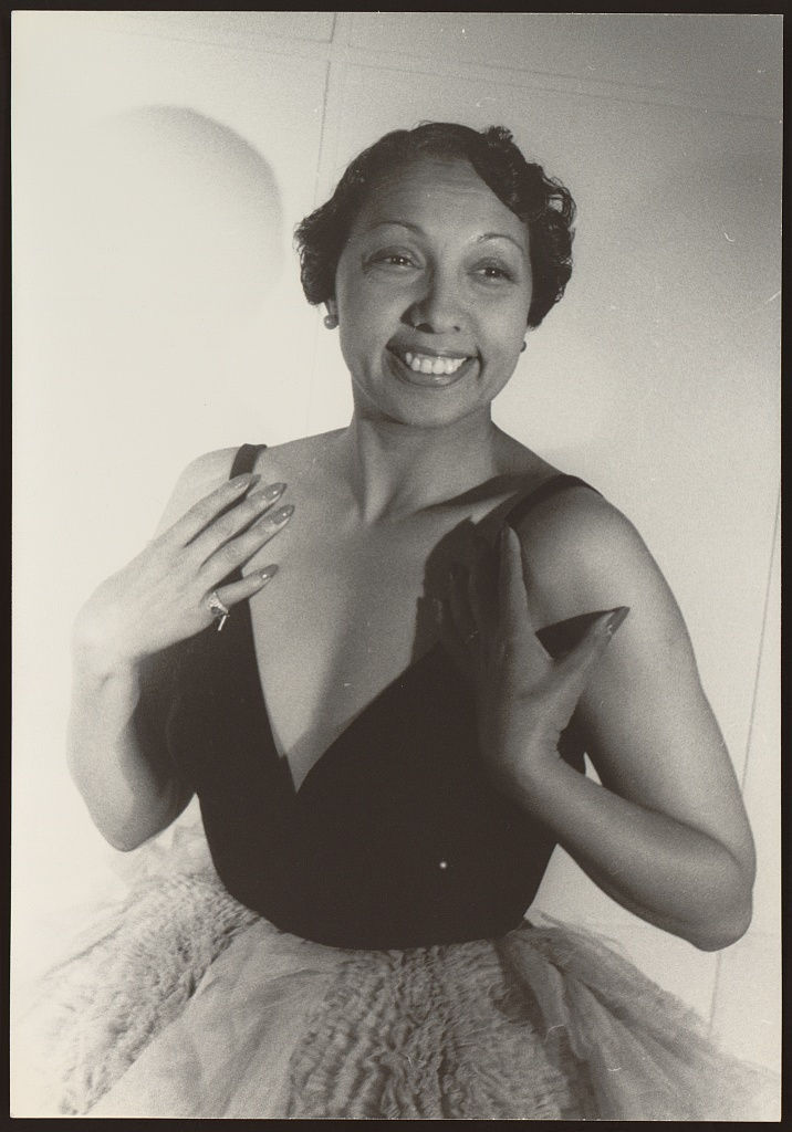 A black-and-white photograph of Josephine Baker, a Black woman who is smiling and wearing a dark dress.