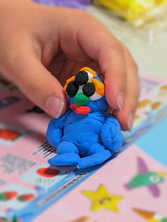 Hand holds blue clay figure with three eyes