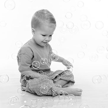 A black and white photography of a little boy who is entranced by floating bubbles