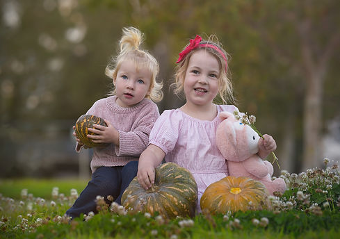 Two toddlers sitting amongst clover flowers and pumpkins