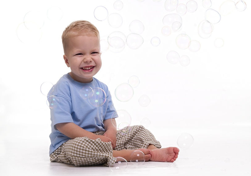 A toddler boy smiling happily as bubbles float around him during a children's portrait session