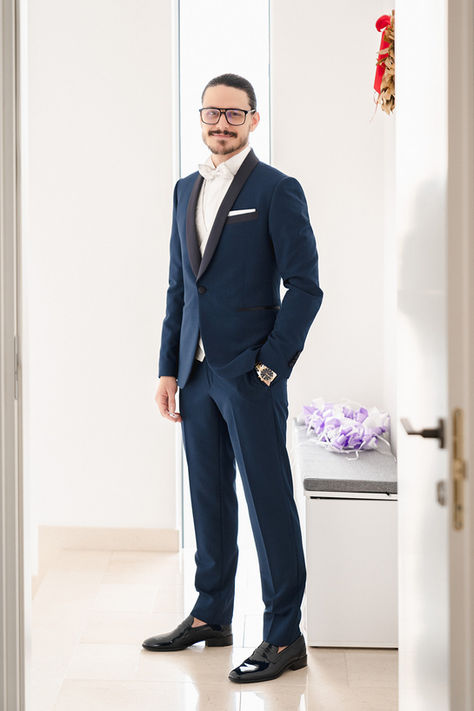 Un uomo in piedi in un completo blu e scarpe bianche accenna un sorriso