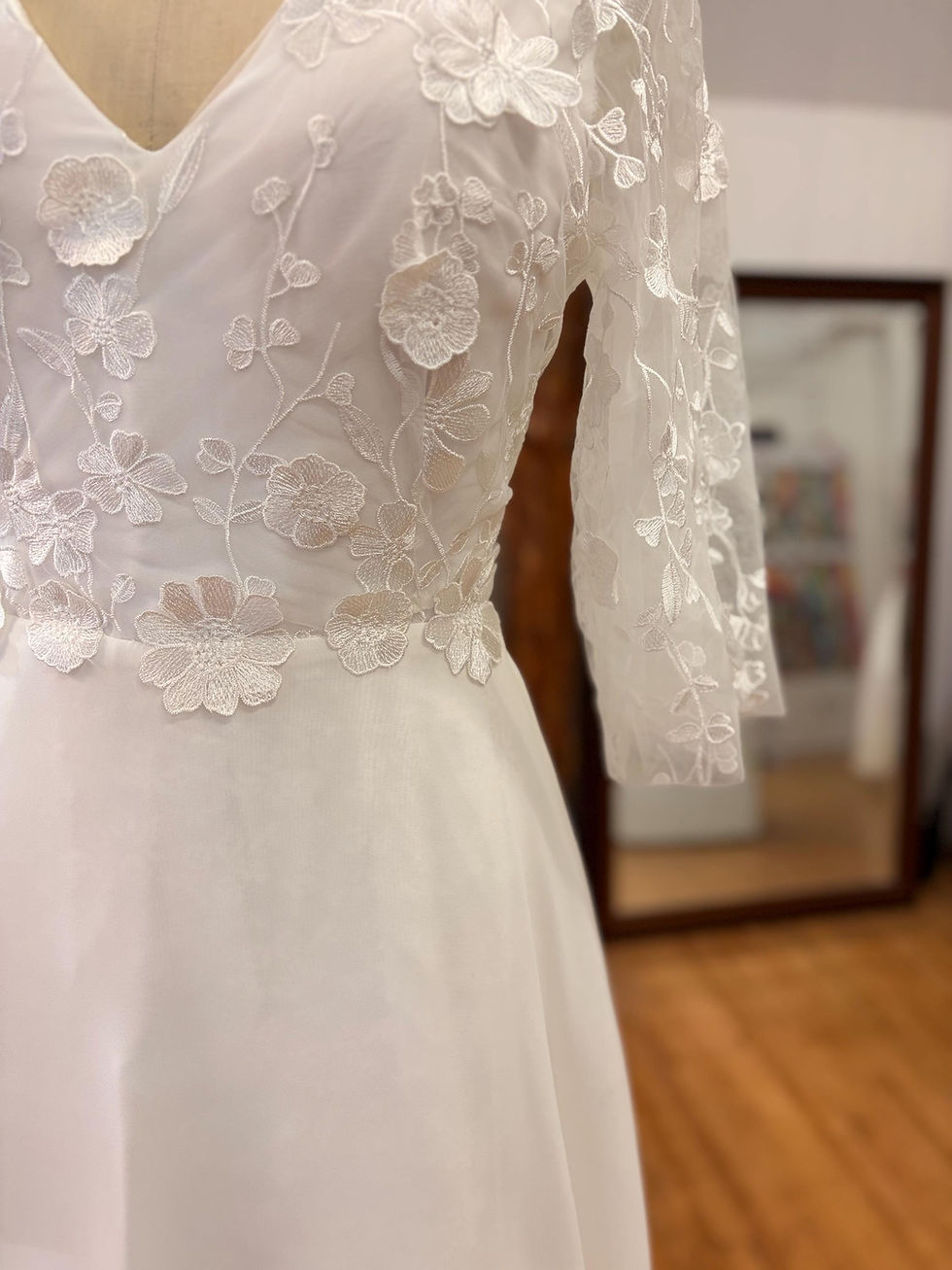 Thumbnail: Détail de la taille et des applications de dentelle 3D fleurie cousues à la main sur la robe de mariée.